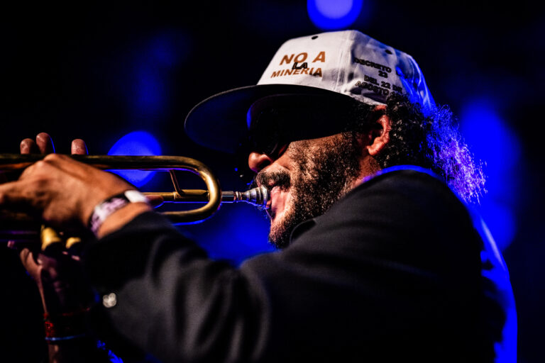 Een muzikant speelt trompet op het podium met een blauwe achtergrond.