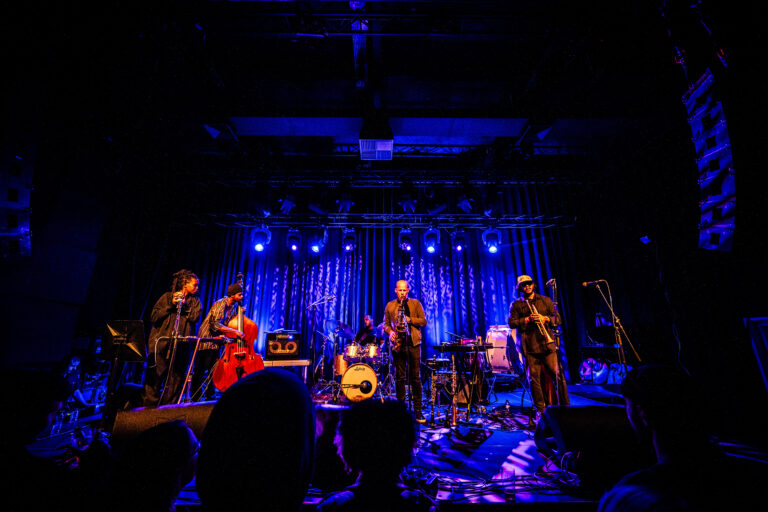 Een band speelt live muziek op een podium verlicht met blauwe lichten.