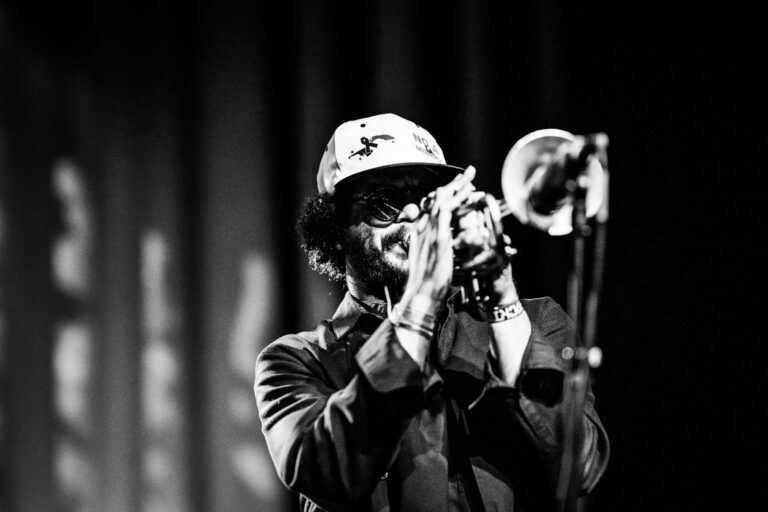 Een muzikant speelt een trompet op een podium in zwart-witstijl.