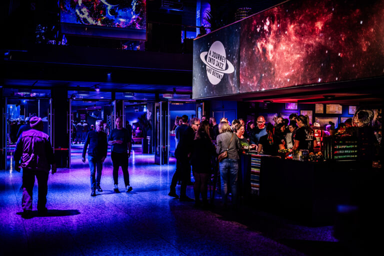 Een levendige bar in een donkere ruimte met kleurrijke verlichting en mensen die interactie hebben.