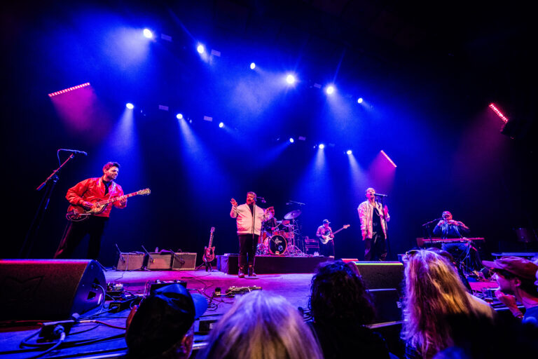 Een band voert op een podium op met felgekleurde verwarming en zangers en muzikanten in actie.