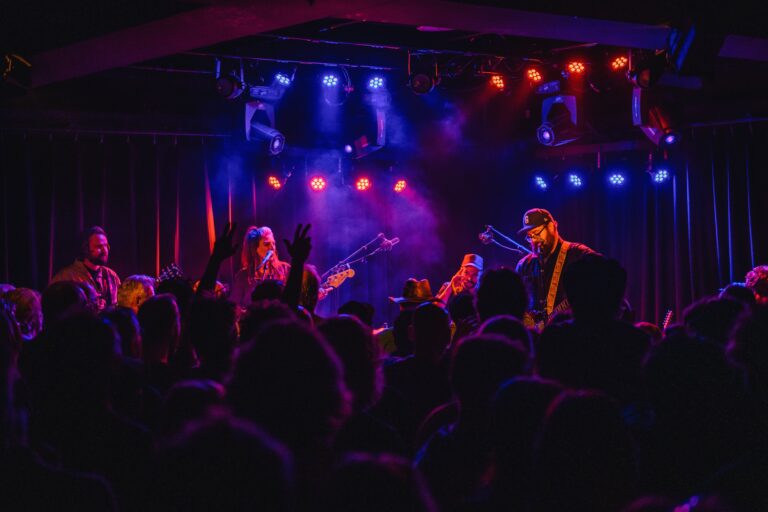 Een live band speelt op een podium met kleurrijke verlichting terwijl een menigte toekijkt.