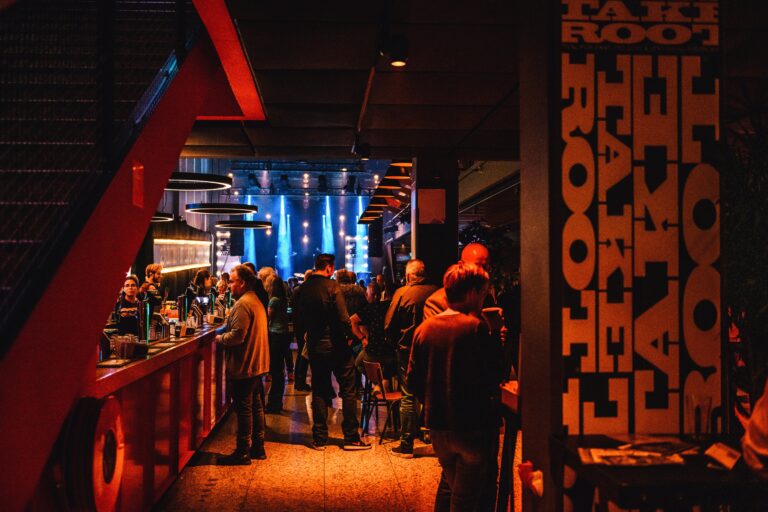 Een drukke bar met bezoekers en een verlichte achtergrond, omringd door modern interieur met warme verlichting.