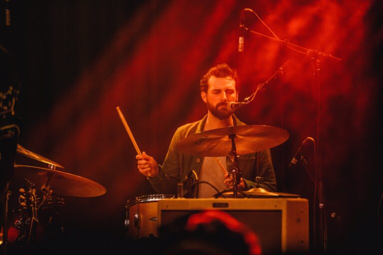 Een drummer speelt op een podium met een warme, rode belichting.