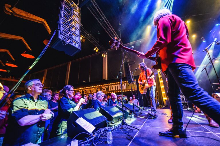 Een band speelt live muziek op een podium voor een enthousiast publiek met kleurrijke verlichting.