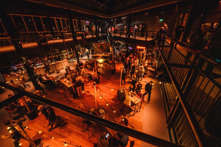 Een drukke ruimte met een warme, uitnodigende sfeer, waar mensen samenkomen in een grotere, stijlvol ingerichte setting.