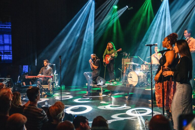 Een liveband staat op een podium met betoverende lichteffecten en een enthousiast publiek.