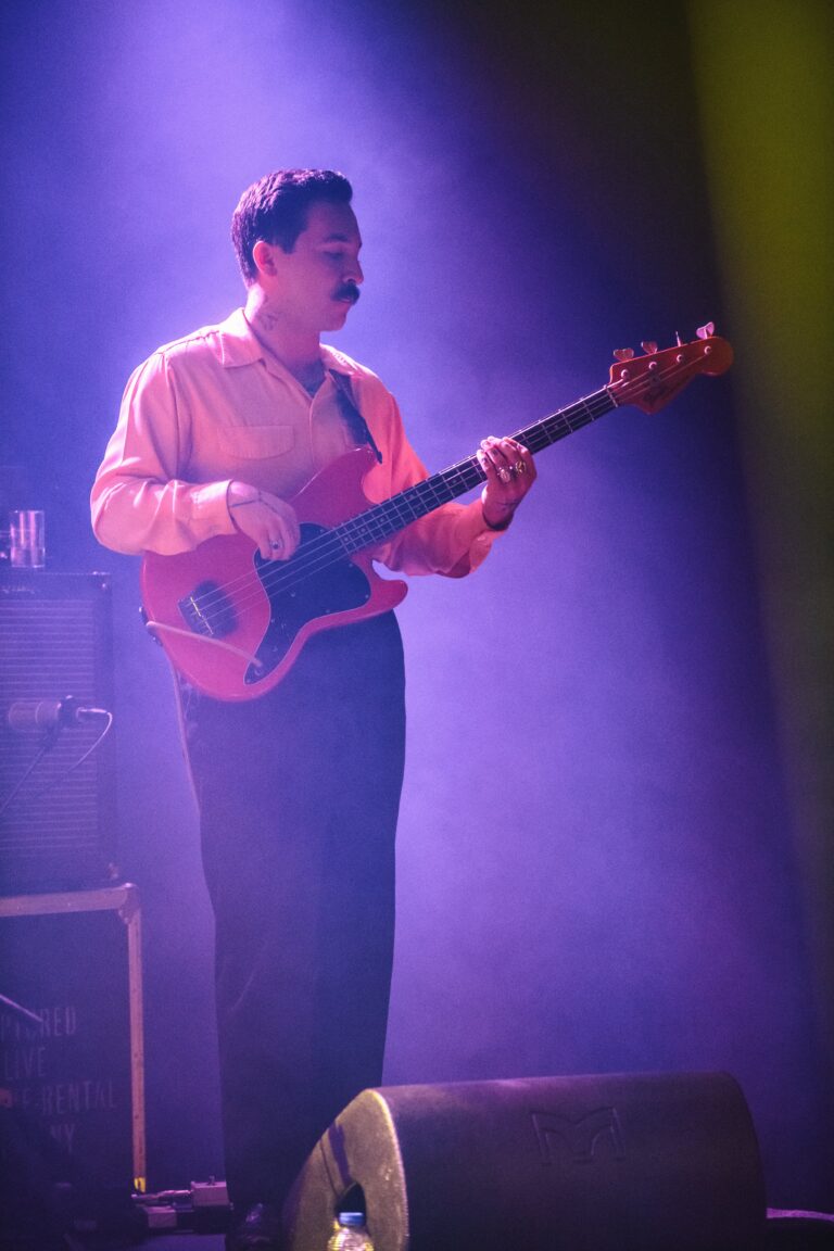 Een muzikant speelt op een rode elektrische gitaar in een verlichte, smoky omgeving.