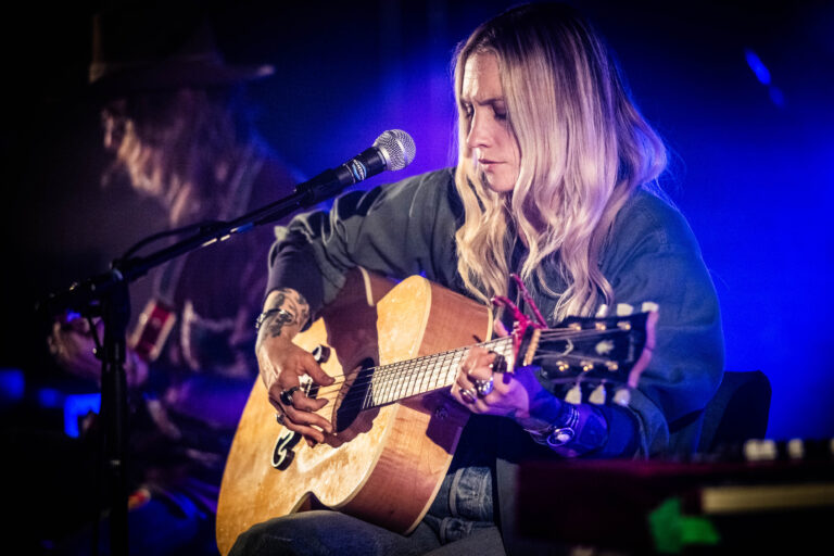Een muzikante speelt een akoestische gitaar op een podium met zachte verlichting.