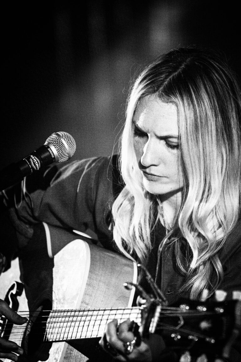 Een muzikante speelt gitaar en zingt, gefocust op haar instrument.