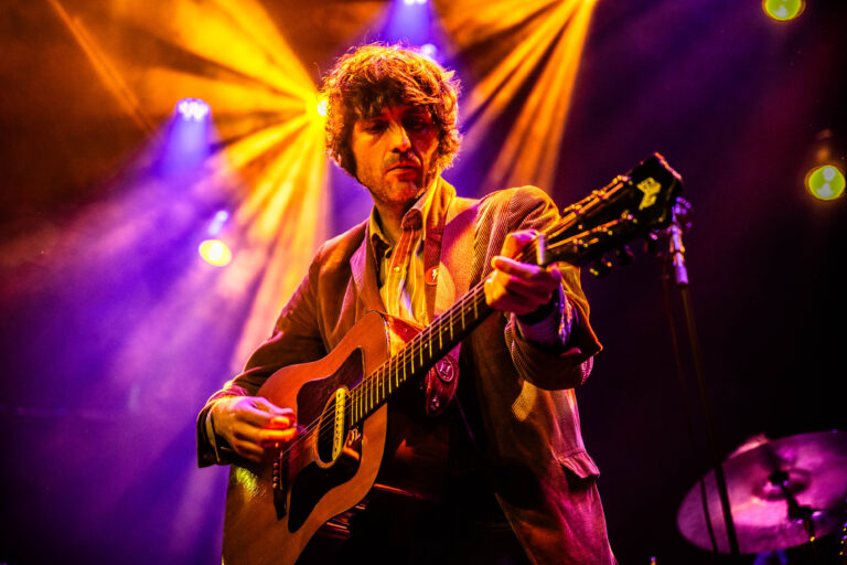 Een muzikant speelt gitaar op een podium met kleurrijke verlichting.