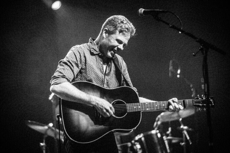 Een muzikant speelt vrolijk gitaar op het podium.