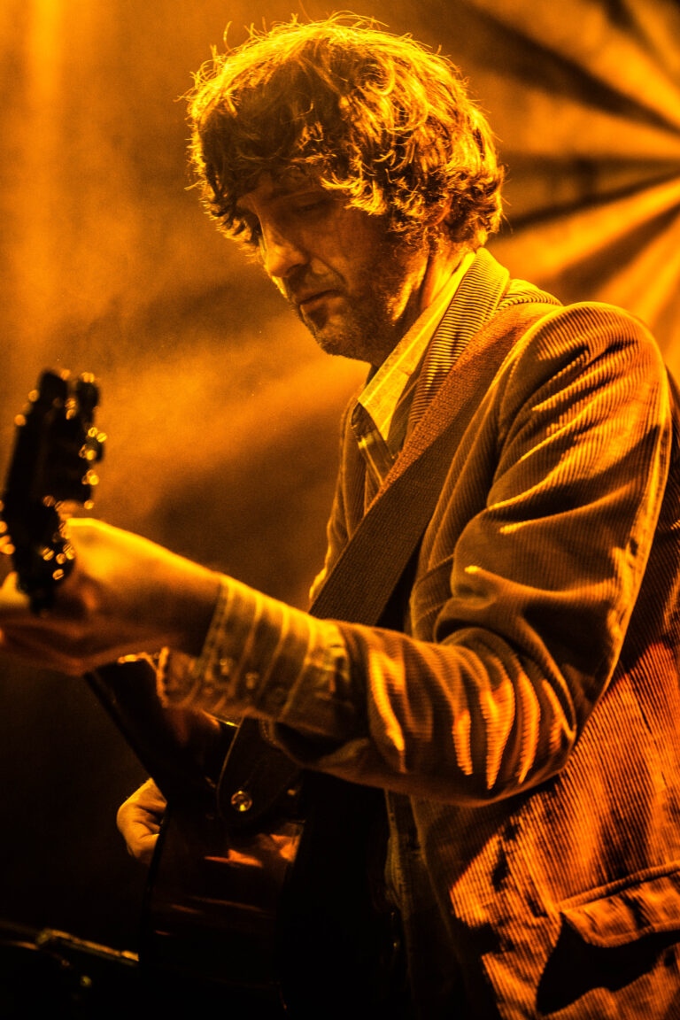 Een muzikant speelt gitaar onder het warme, gouden licht van een podium.