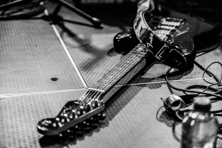 Een elektrische gitaar ligt op een vloerbedekking tussen muziekapparatuur.