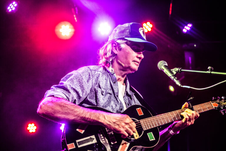 Een muzikant speelt gitaar op een podium met kleurrijke verlichting.