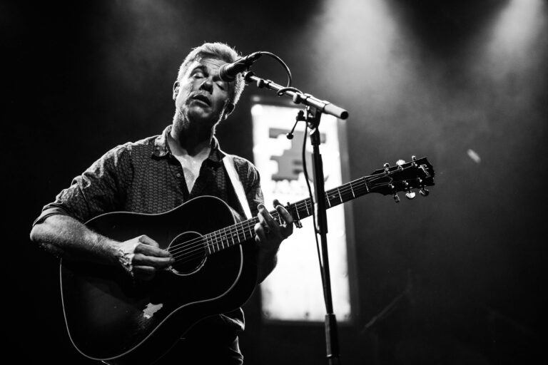 Een muzikant speelt een akoestische gitaar en zingt tijdens een optreden met een hazy achtergrond.