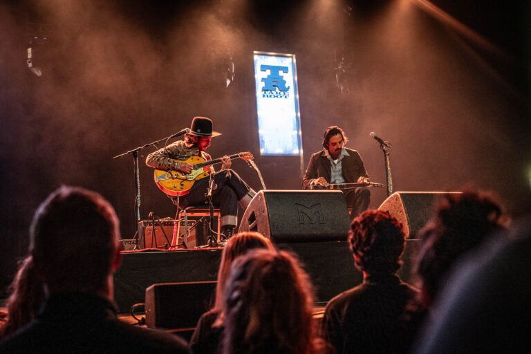 Twee muzikanten geven een live optreden op een podium met zachte verlichting.
