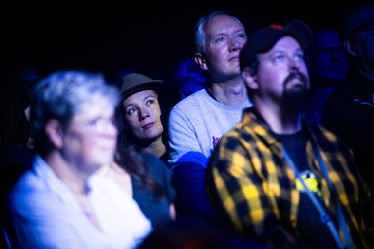 Een groep mensen kijkt aandachtig naar een optreden in een dimverlichte omgeving.