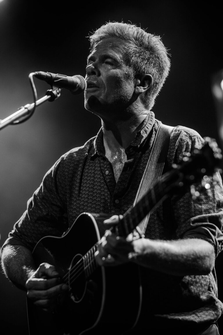 Een muzikant die een gitaar speelt en zingt in een liveoptreden met een microfoon voor zich.