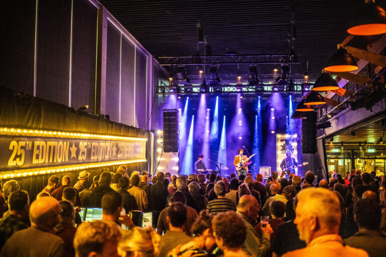 Een druk concert in een sfeervolle zaal met kleurrijke verlichting en een band op het podium.