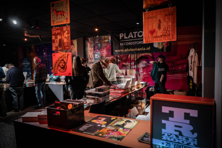 Een drukke beursstand met kleurrijke affiches en bezoekers die zich verdiepen in de aangeboden materialen.