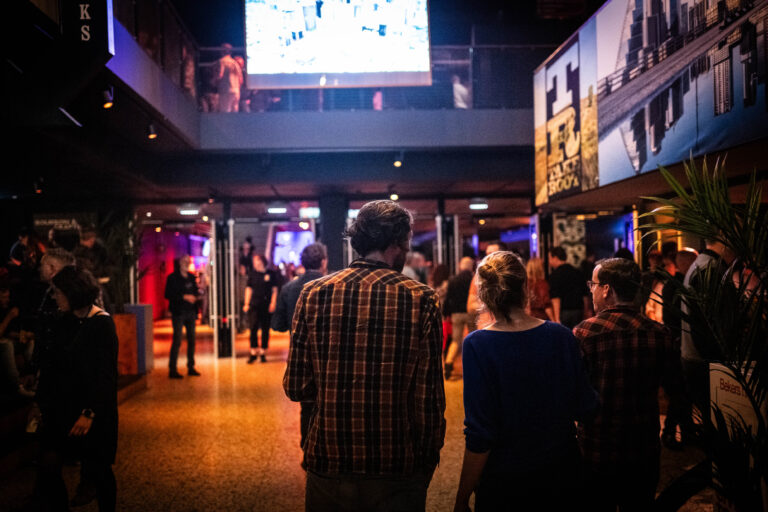 Een groep mensen kijkt naar een scherm in een sfeervol verlichte ruimte met kunstwerken aan de muren.