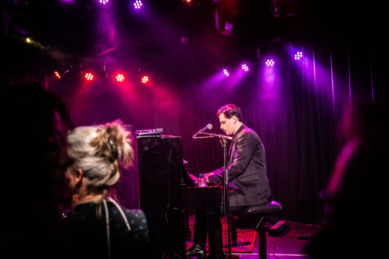 Een muzikant speelt piano op een podium met kleurrijke verlichting.