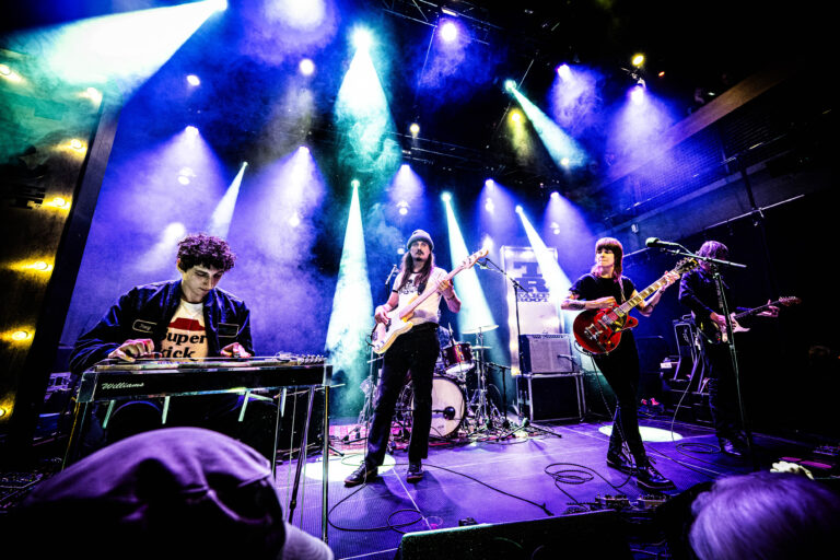 Een band speelt live op een podium met kleurrijke lichten en enthousiaste energie.