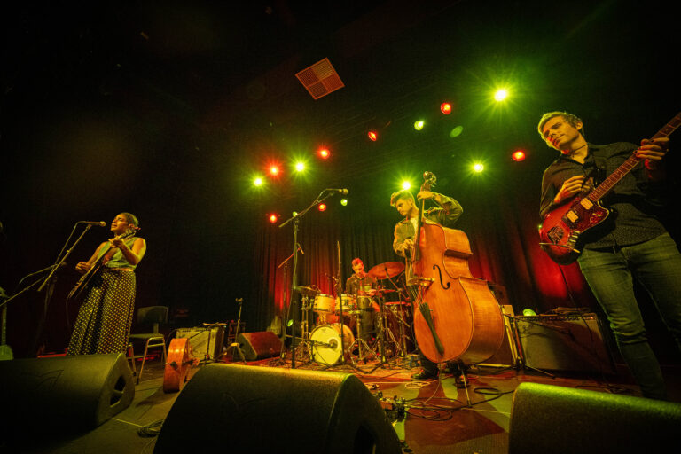 Een band speelt live op een podium met kleurrijke verlichting.