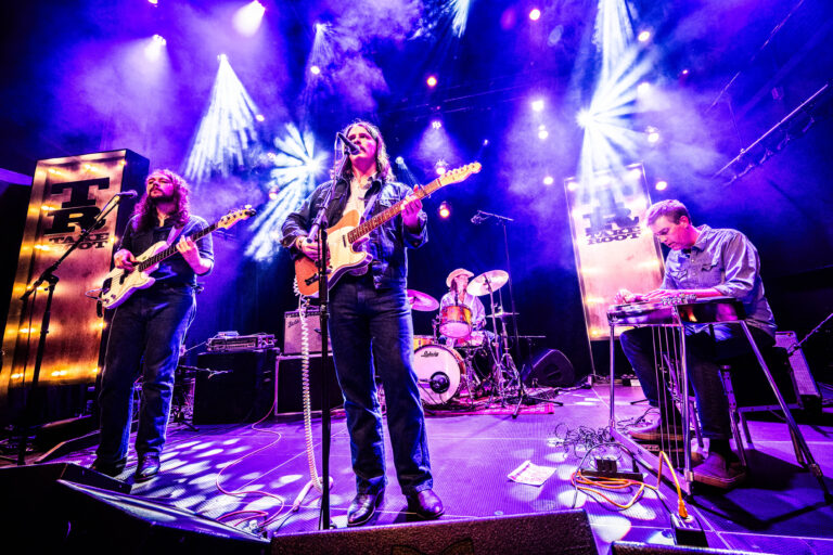 Een band performt op een podium met kleurrijke verlichting en een enthousiast publiek.
