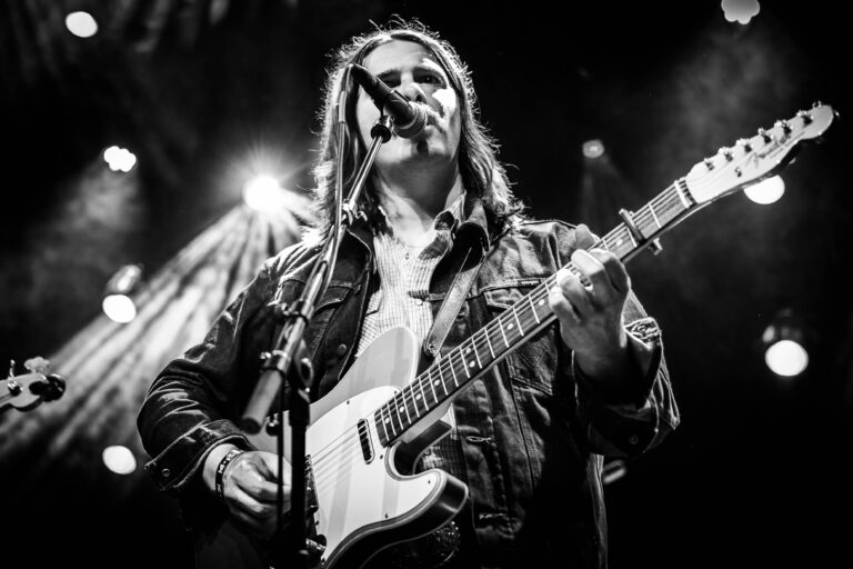 Een muzikant met een elektrische gitaar zingt in het licht van het podium.