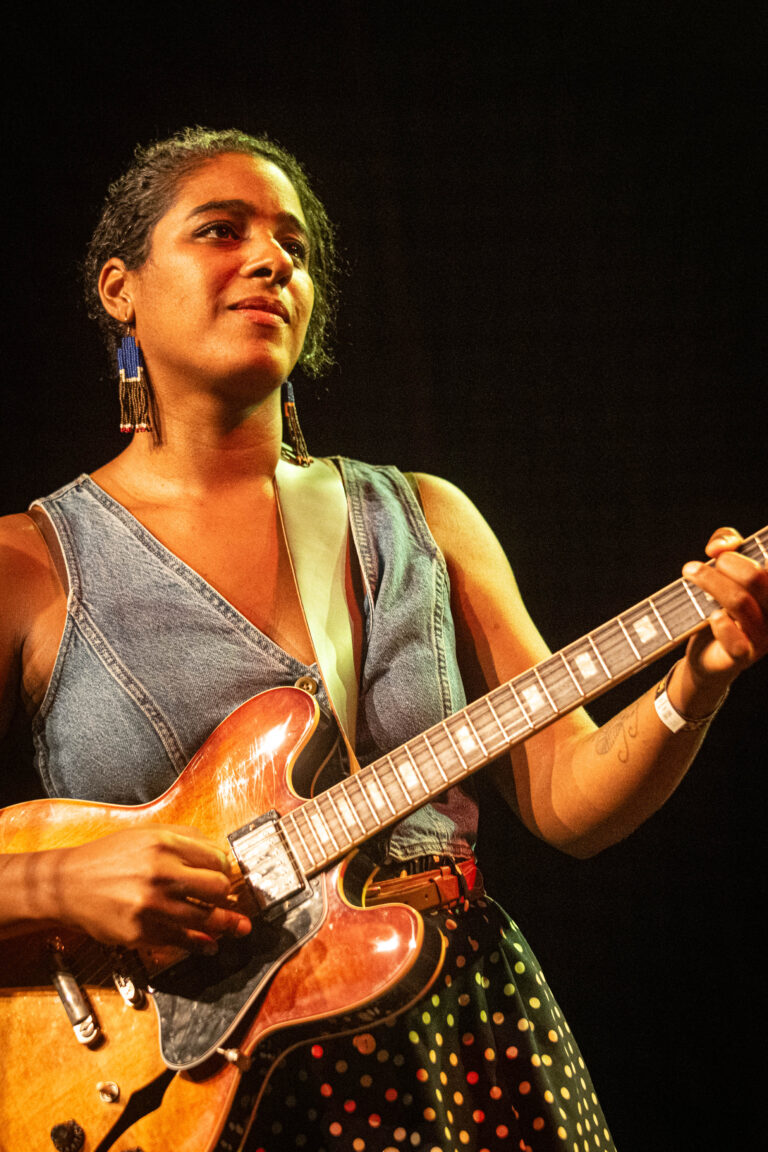 Een vrouw speelt gitaar op het podium, met een focus op haar expressieve houding.
