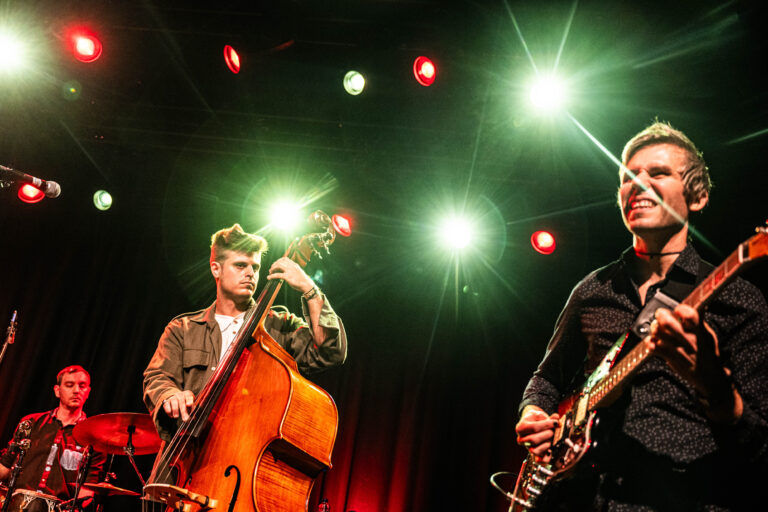Twee muzikanten spelen live op een podium met felgekleurde lichten.