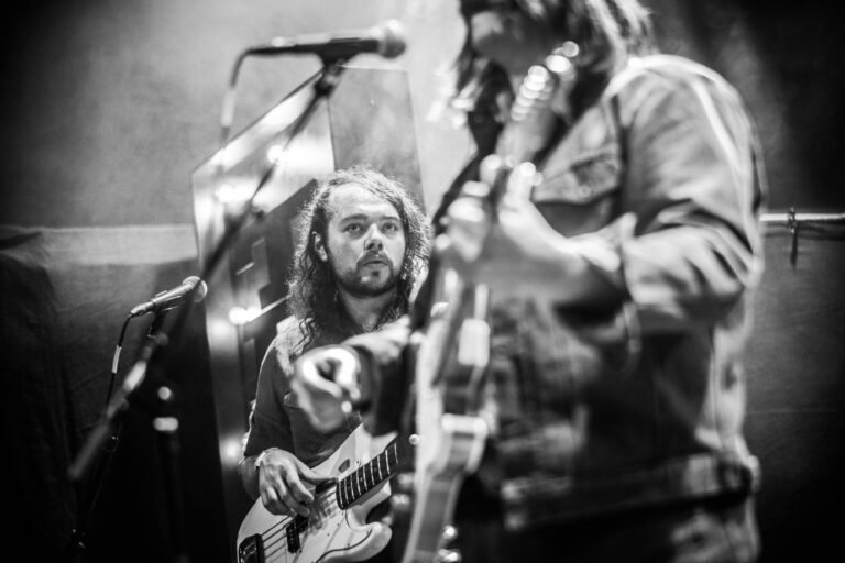 Twee muzikanten optreden op een podium, met de focus op een gitarist en een bassist die betrokken zijn bij hun uitvoering.