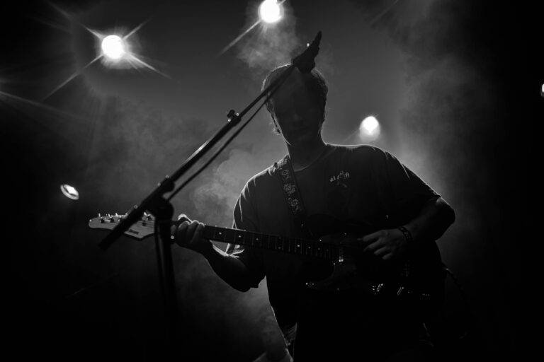 Een silhouette van een muzikant die een gitaar speelt op een podium, omringd door sfeerverlichting en rook.