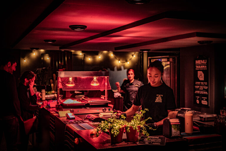 Twee mensen werken in een sfeervol verlichte keuken met planten en decoratieve verlichting.