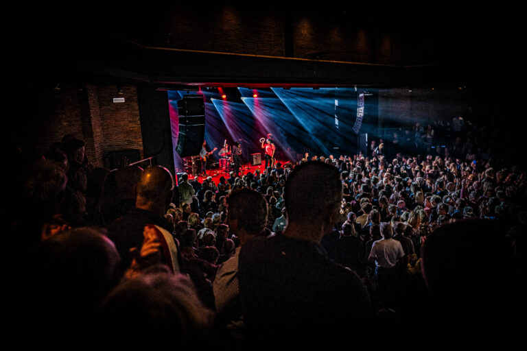 Een drukbezocht concert met kleurrijke lichten en een band die optreedt op het podium.