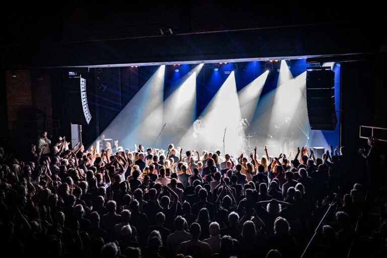 Een druk bezocht concert met mensenmassa onder kleurrijke lichten op het podium.
