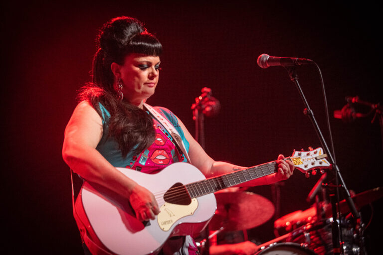 Een muzikant met een opvallende haardos speelt gitaar op het podium.