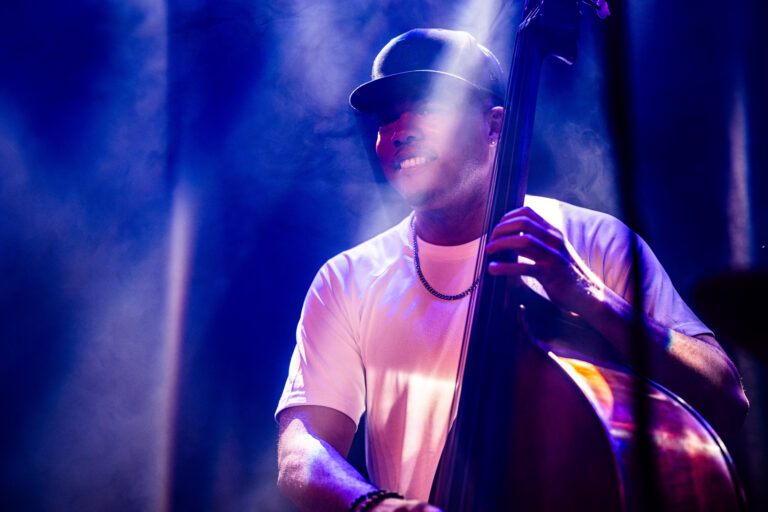 Een muzikant bespeelt een contrabas terwijl hij in het licht van de spots staat.