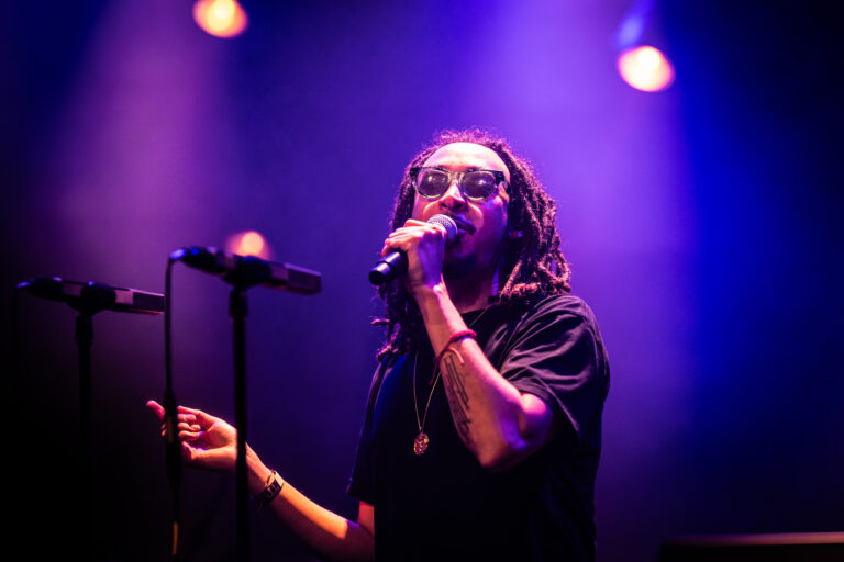 Een muzikant zingt op een podium, omringd door paarse lichten.