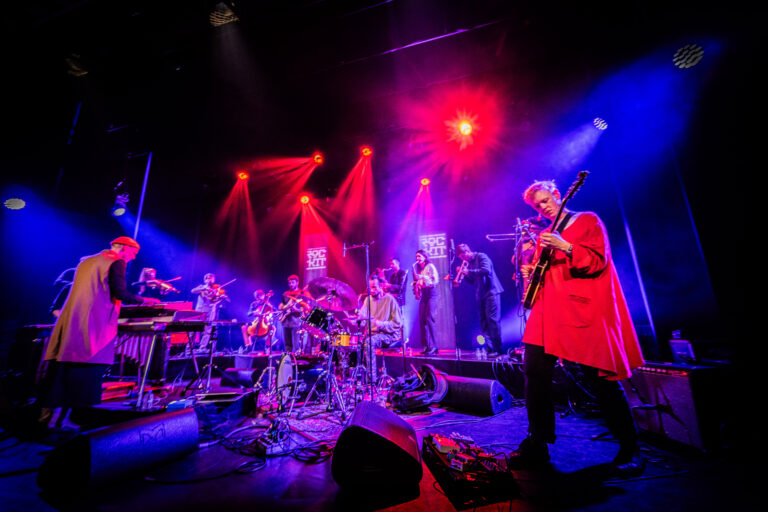 Een band speelt op een podium, omringd door kleurrijke verlichting.