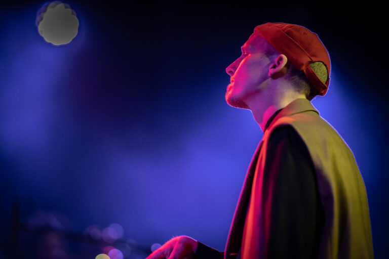 Een persoon met een rode pet staat in een sfeervolle, donker verlichte omgeving.