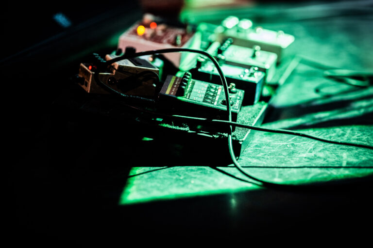 Een close-up van muziekpedalen met kabels in een grijsgroene lichteffect.