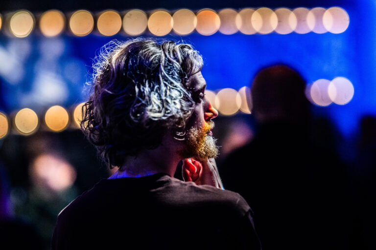 Een persoon met krullend haar kijkt naar een kleurrijke achtergrond met sfeerverlichting.