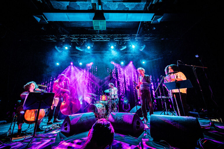 Een band speelt live op een podium met kleurrijke lichten en een dynamische sfeer.