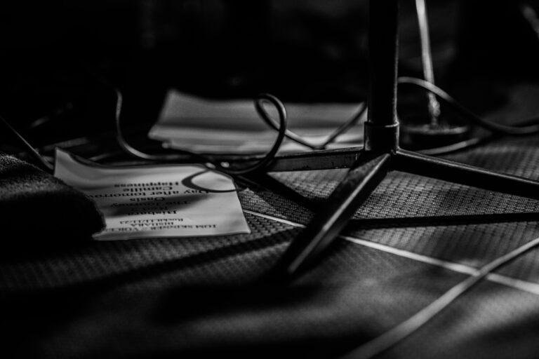 Een close-up van een microfoonstandaard met papieren en kabels op de vloer.