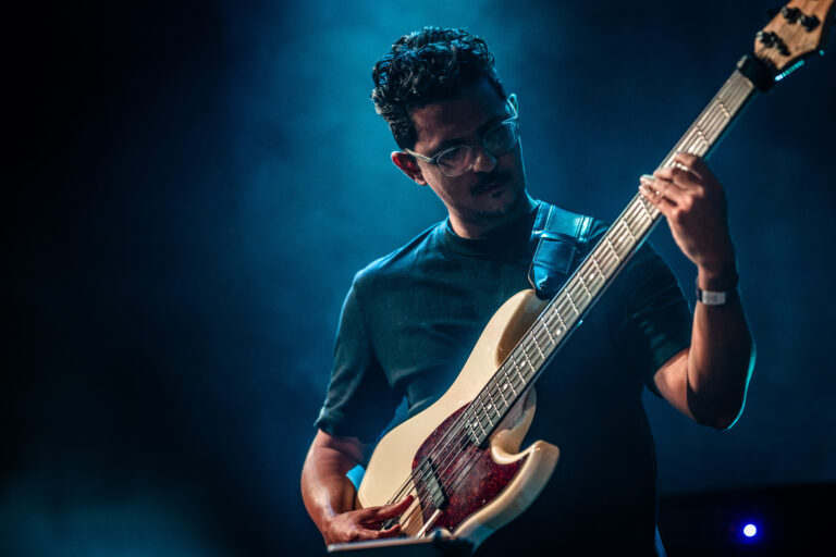 Een muzikant speelt een elektrische gitaar op een podium, omgeven door een zachte blauwe verlichting.