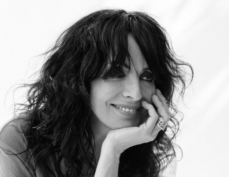 Zwart wit foto van Duitse zangeres en popicoon Nena, die lachend haar hoofd op haar hand rust.