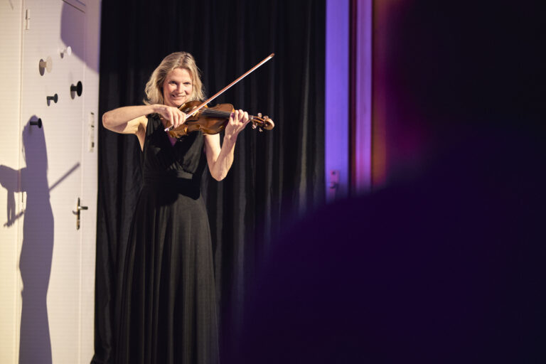 Vrouw in een lange zwarte jurk die viool speelt.